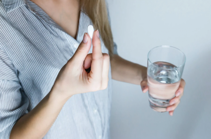 A woman is holding a pill from a medical courier service in San Angelo and a glass of water